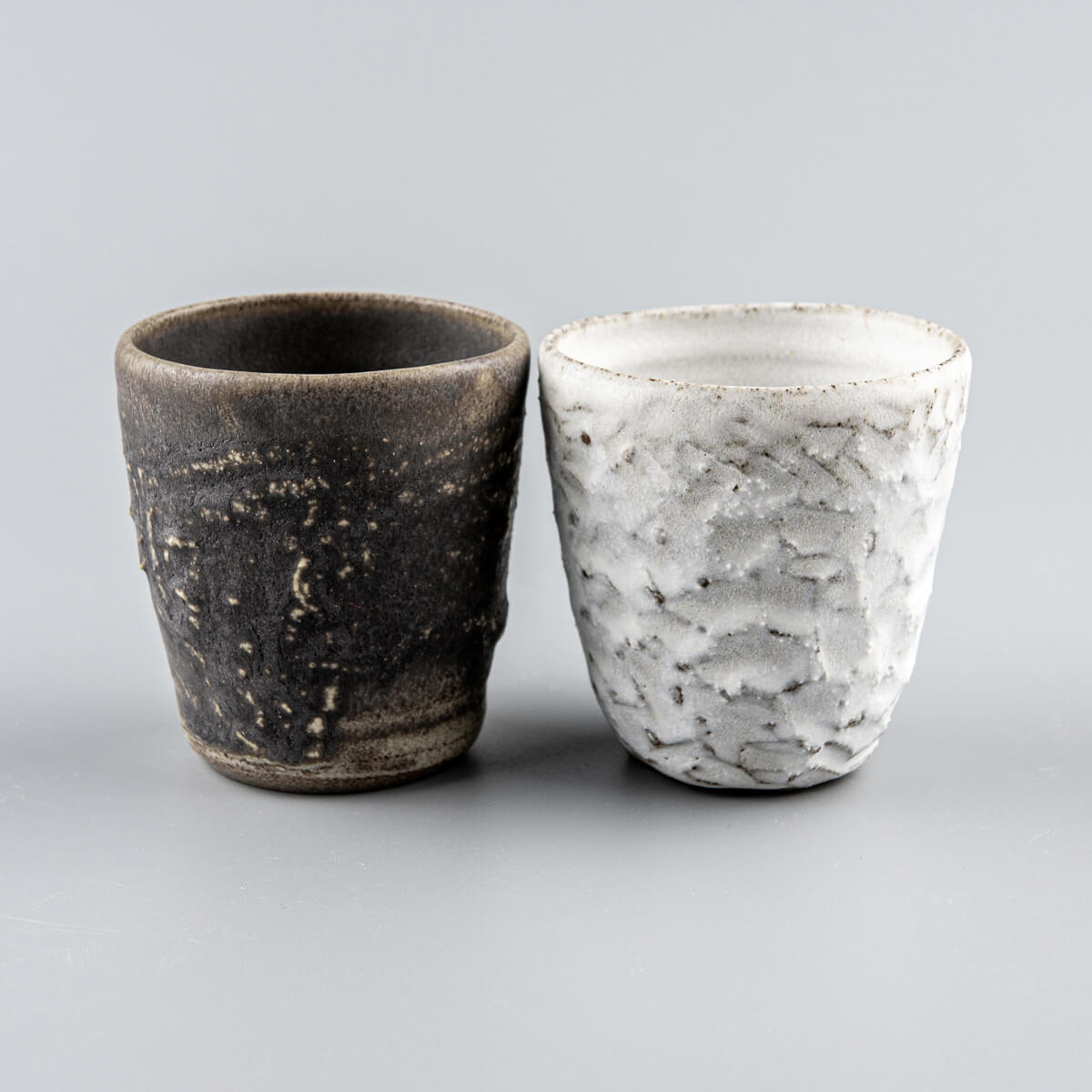 Handcrafted stoneware mug set with textured olive-green glaze and matte white carved finish for coffee and tea rituals.