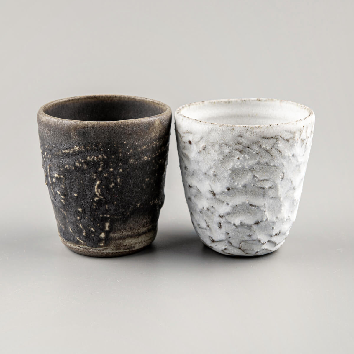 Handcrafted stoneware mug set with textured olive-green glaze and matte white carved finish for coffee and tea rituals.