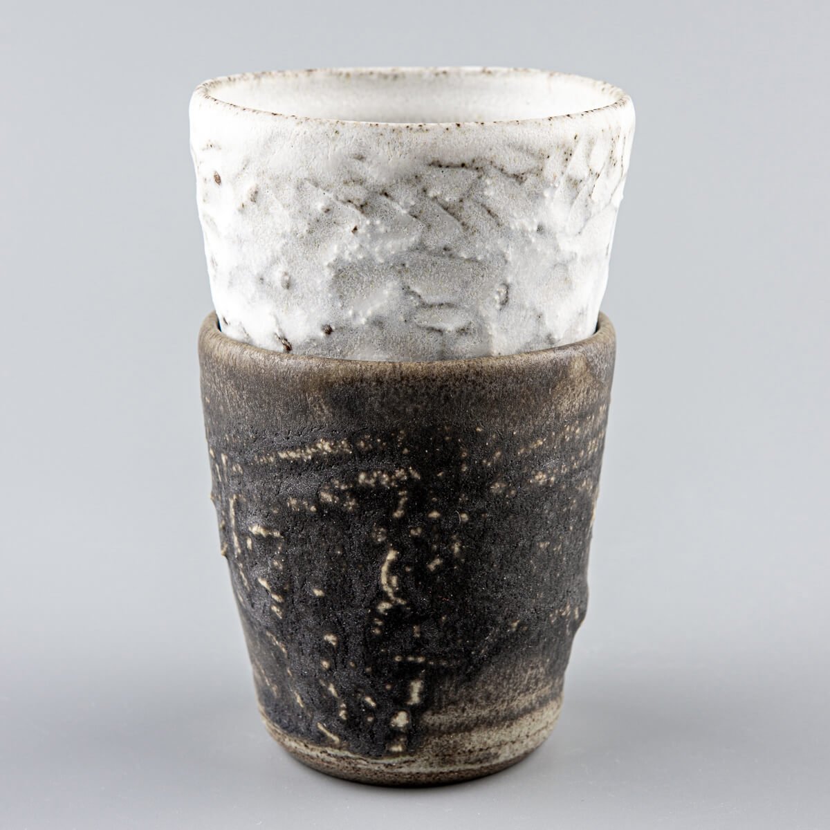 Paired stoneware mugs in contrasting dark and white glazes, crafted for home, restaurant, and luxury table settings.