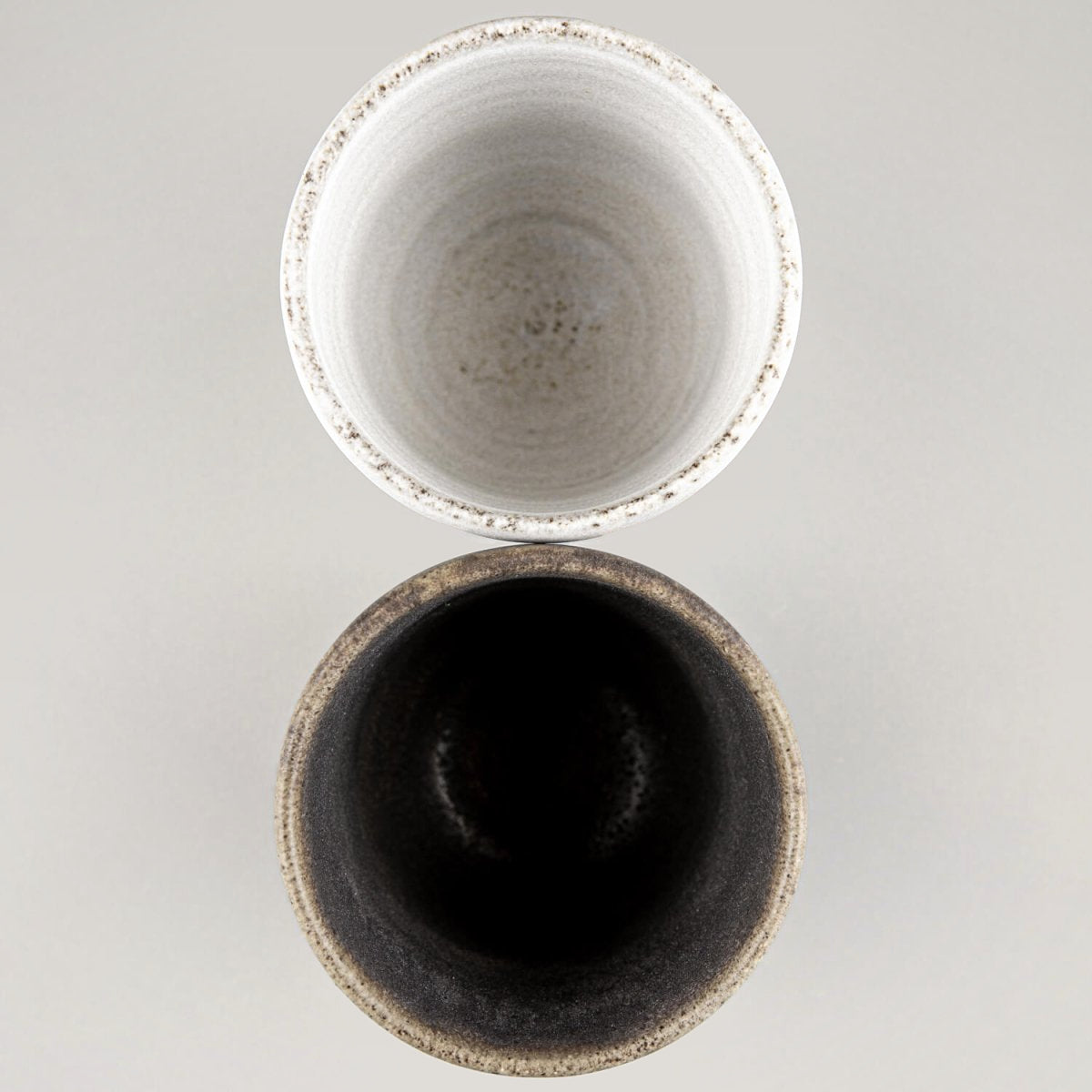 Handmade pottery cups, top view, showcasing white matte and dark olive glaze contrast for fine dining.