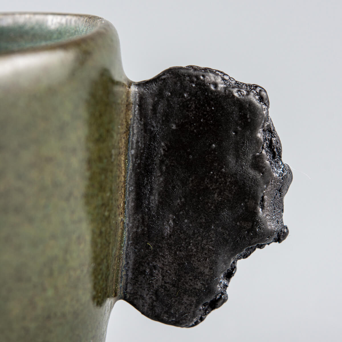 Close-up of unique raw black clay handle on handmade pottery mug for interior design and collectors.