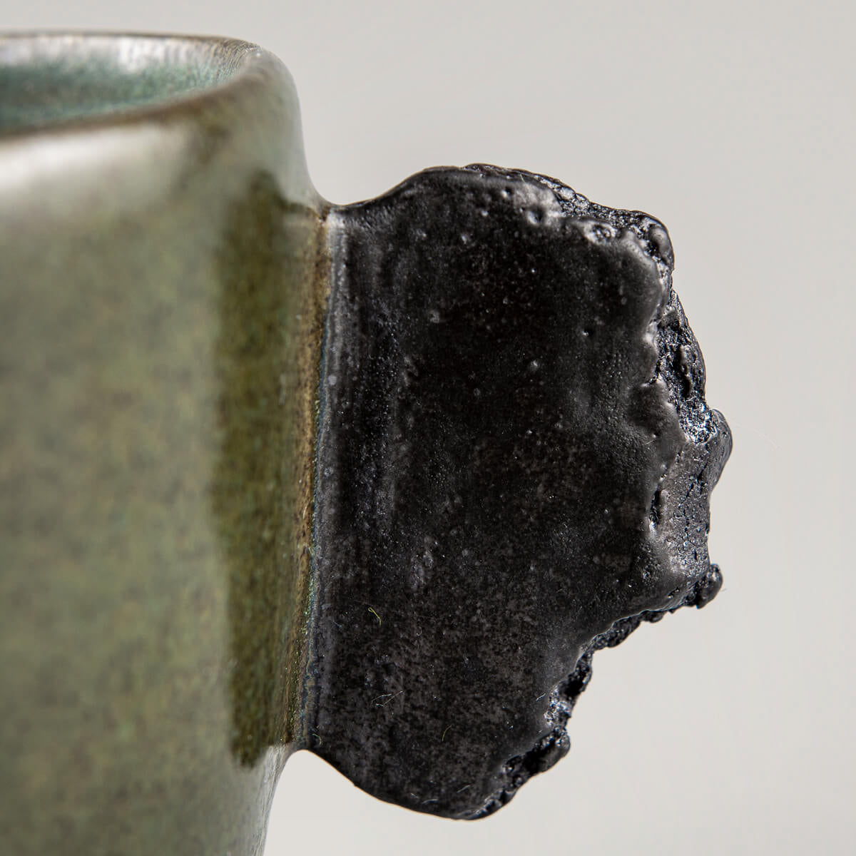 Close-up of unique raw black clay handle on handmade pottery mug for interior design and collectors.