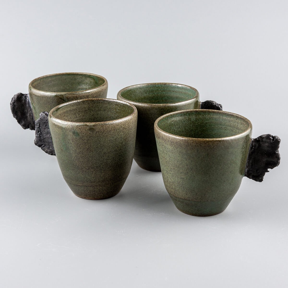 Handcrafted pottery mugs set with matte green glaze and raw black clay handles for fine dining and boutique hotels.