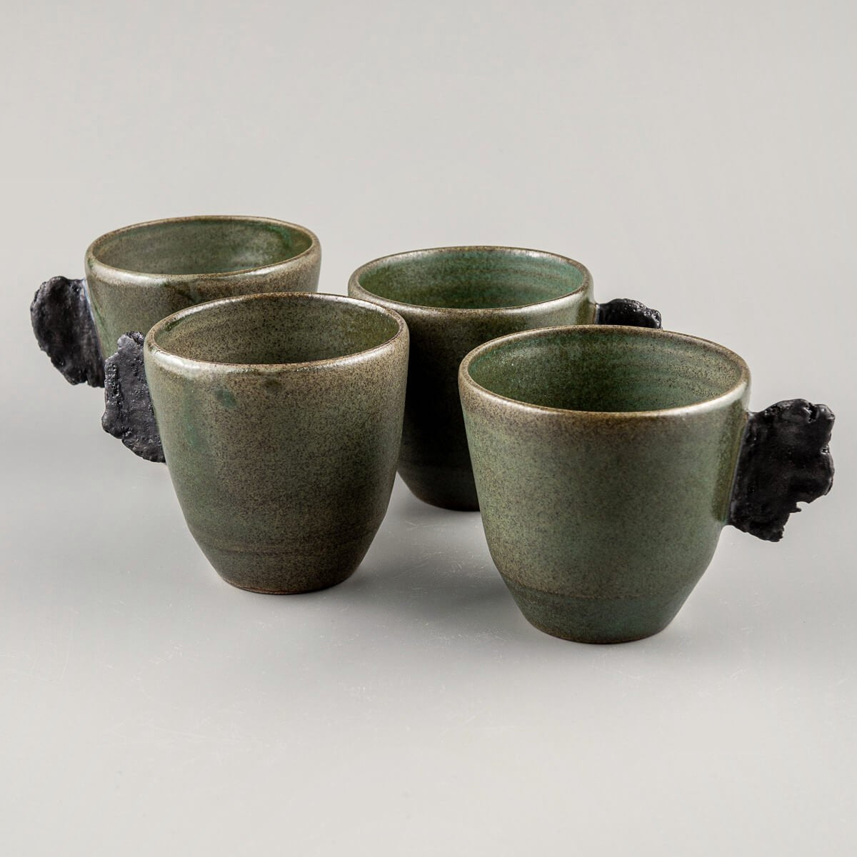 Handcrafted pottery mugs set with matte green glaze and raw black clay handles for fine dining and boutique hotels.
