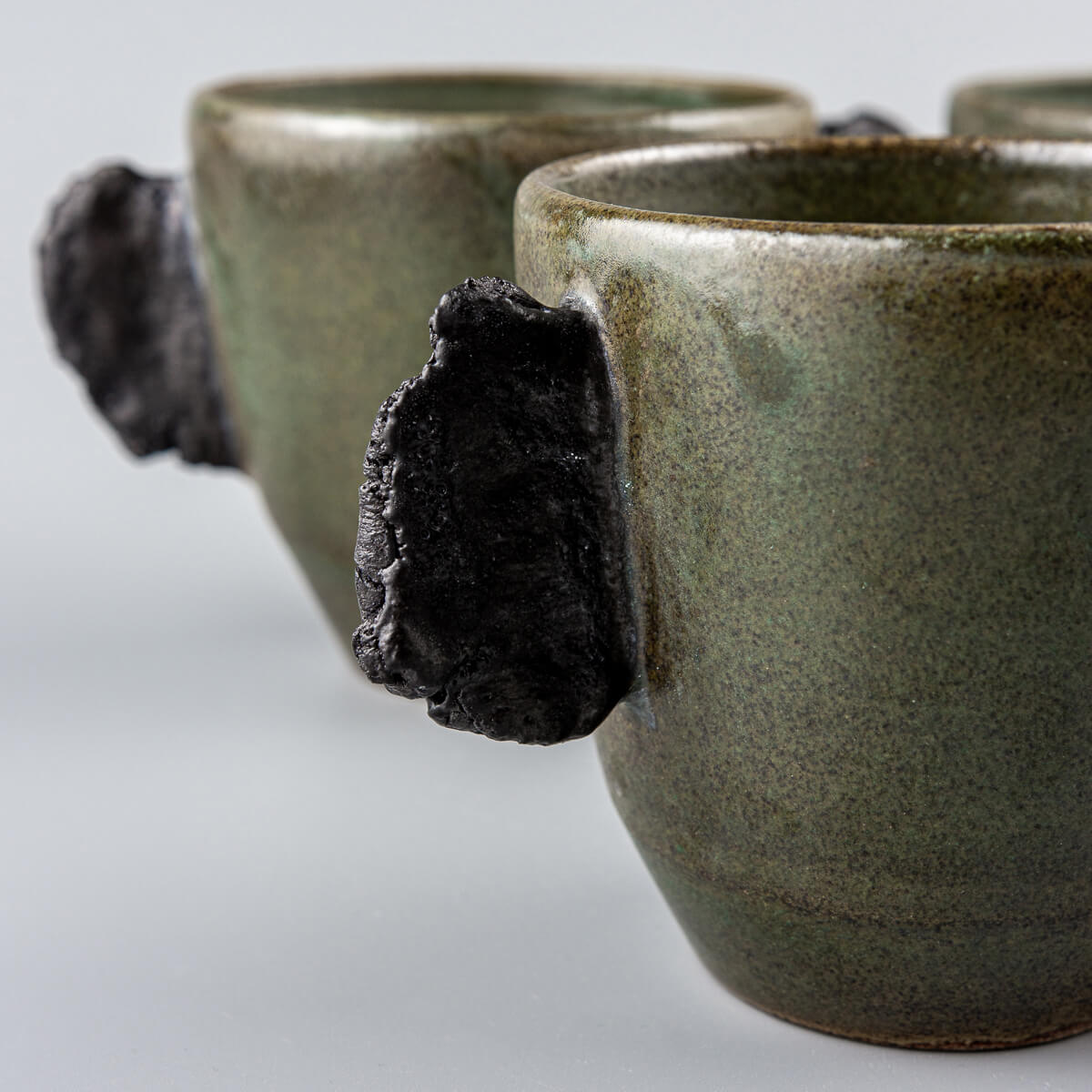 Artisanal ceramic mugs set in earthy green tones, designed for fine dining restaurants and boutique hotel tableware.