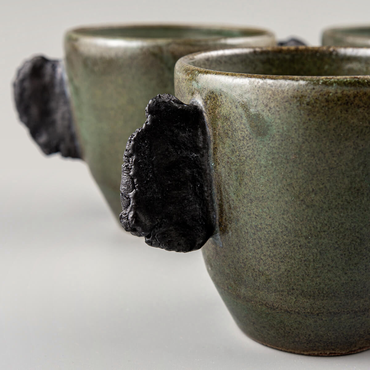 Artisanal ceramic mugs set in earthy green tones, designed for fine dining restaurants and boutique hotel tableware.