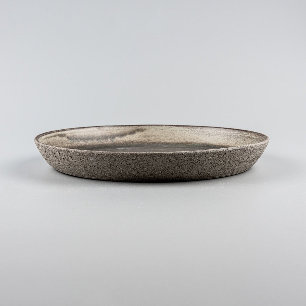 Side view of handcrafted ceramic plate with unglazed dark stoneware exterior for fine dining presentation.
