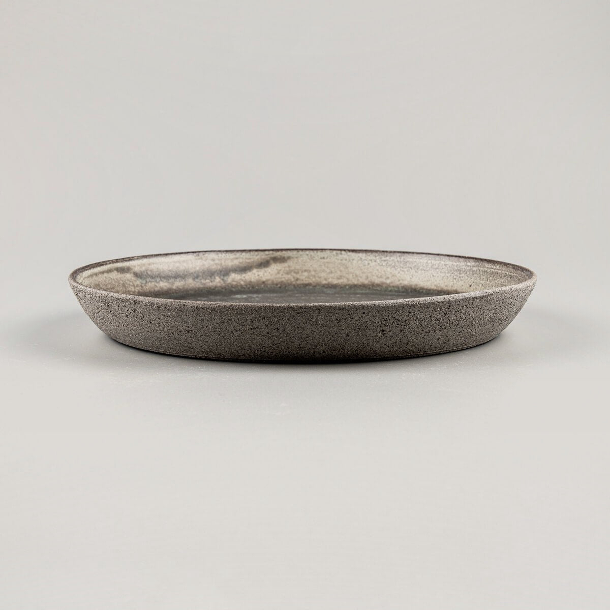 Side view of handcrafted ceramic plate with unglazed dark stoneware exterior for fine dining presentation.