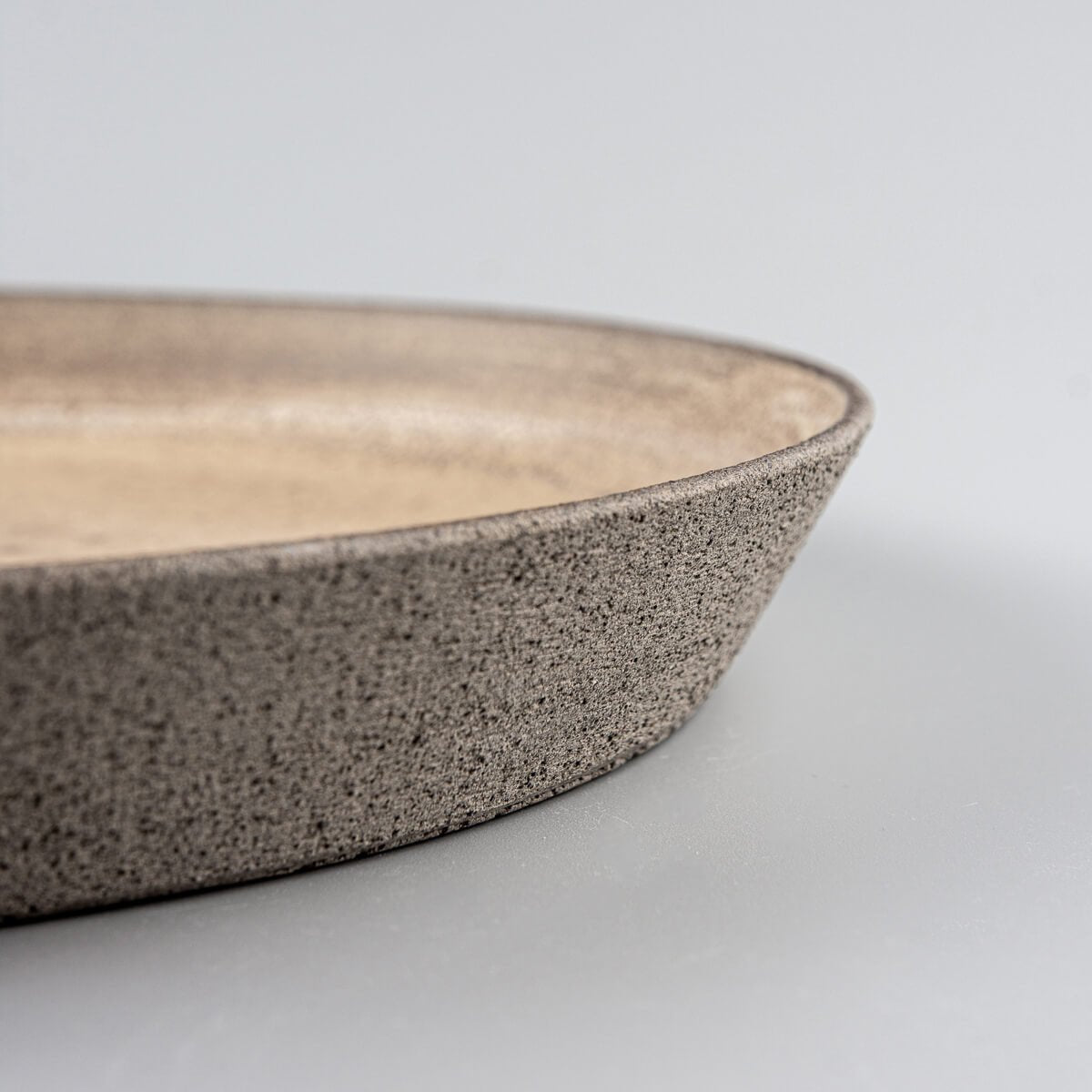 Stoneware dinner plate with textured unglazed exterior in dark clay for luxury dining settings.