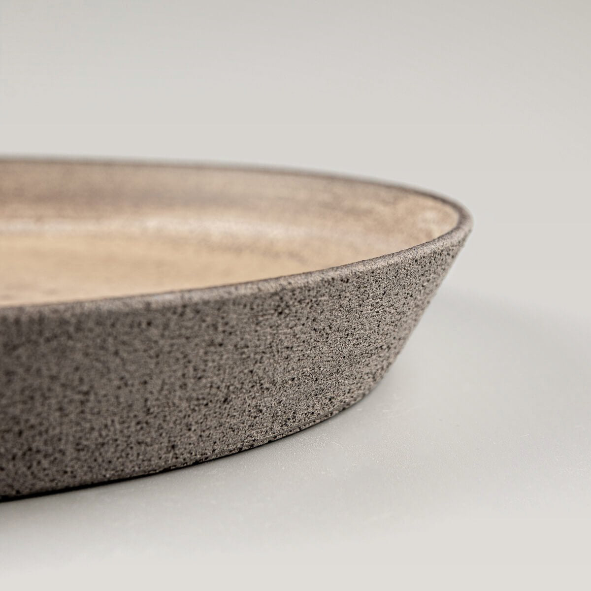 Stoneware dinner plate with textured unglazed exterior in dark clay for luxury dining settings.