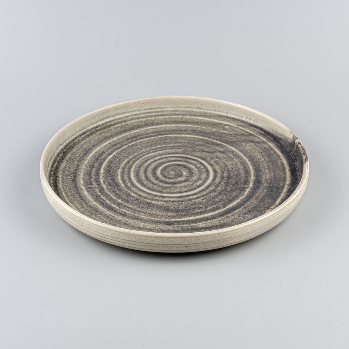 Side view of artisanal ceramic plate with gently curved edges and refined spiral pattern.