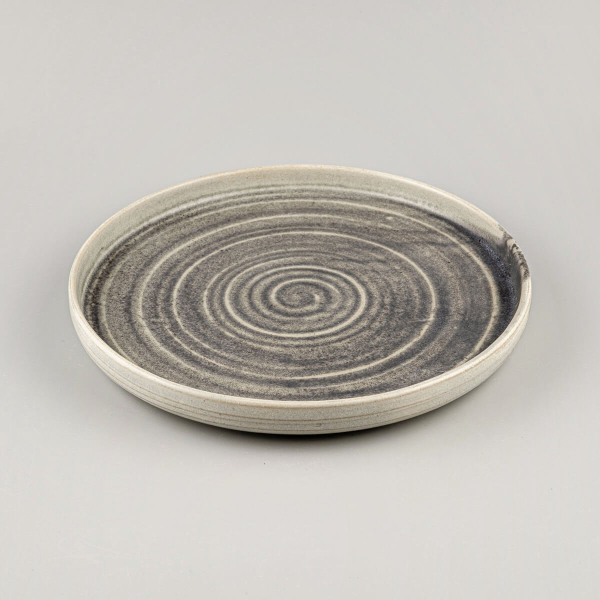 Side view of artisanal ceramic plate with gently curved edges and refined spiral pattern.