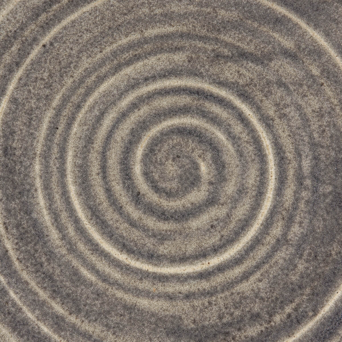 Close-up of a handcrafted ceramic plate showcasing a spiral motif and refined matte glaze.