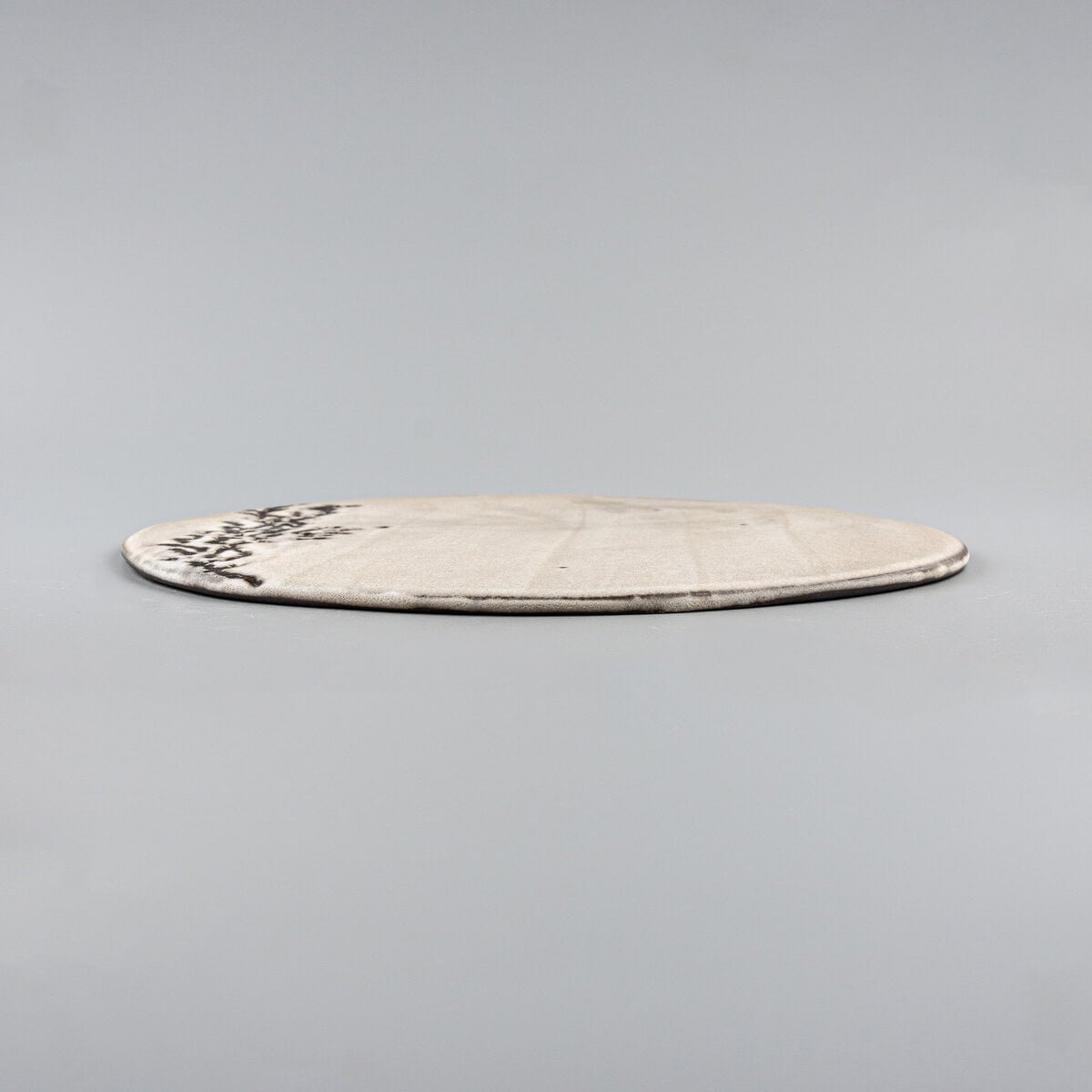 Side view of flat, unique ceramic plate in matte white glaze with subtle hand-textured design for luxury dining.