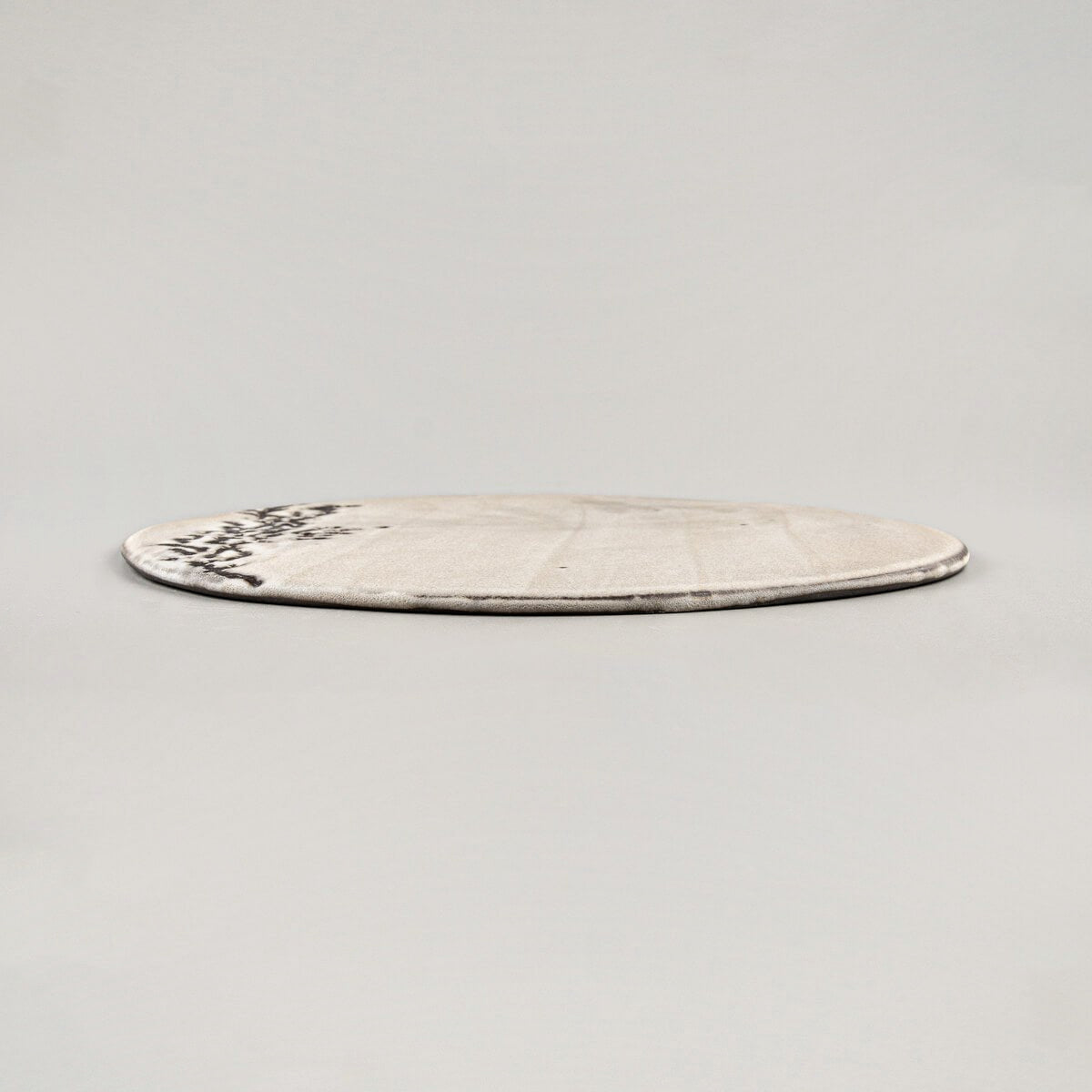 Side view of flat, unique ceramic plate in matte white glaze with subtle hand-textured design for luxury dining.