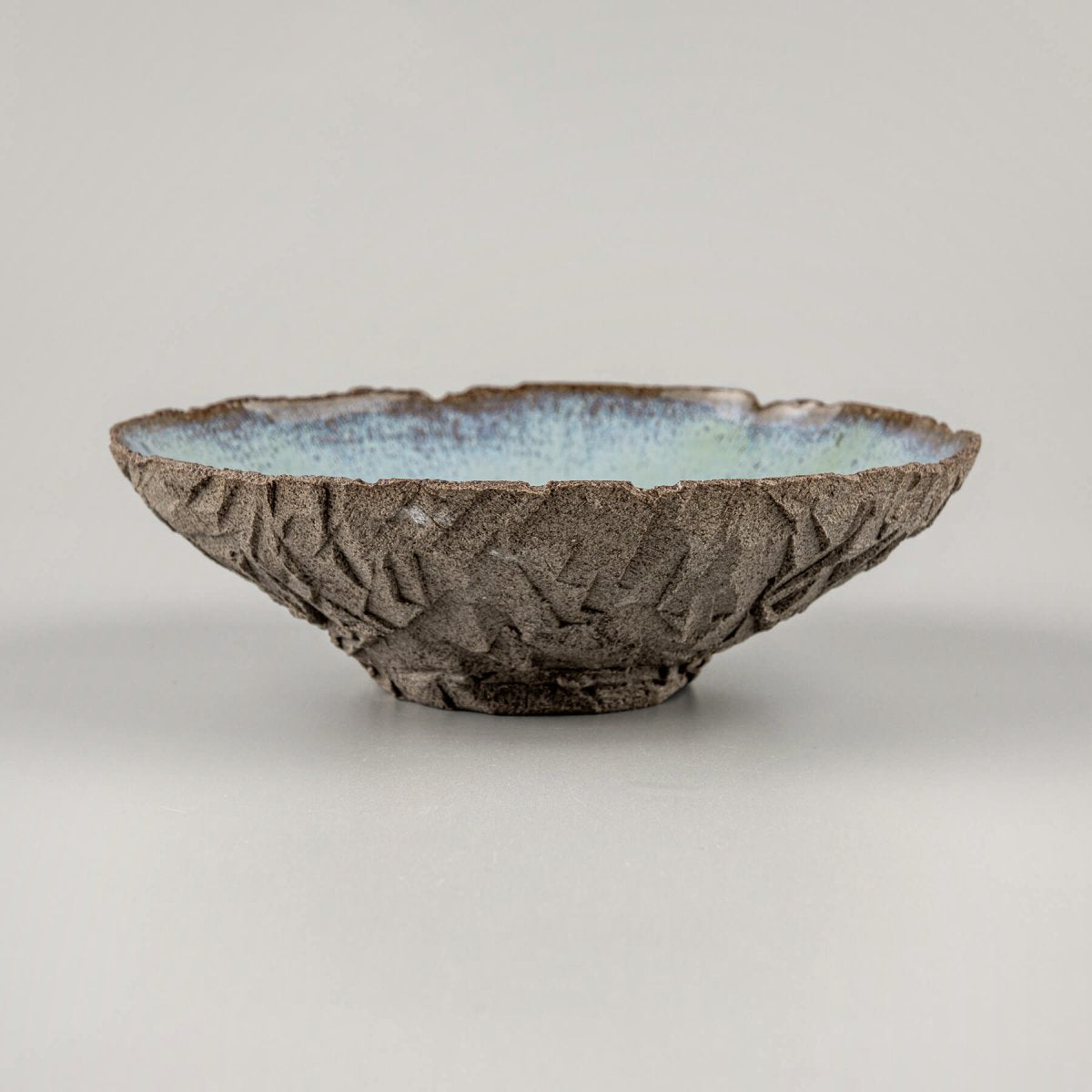 Artisan ceramic bowl with carved dark stoneware texture and glossy blue glazed interior.
