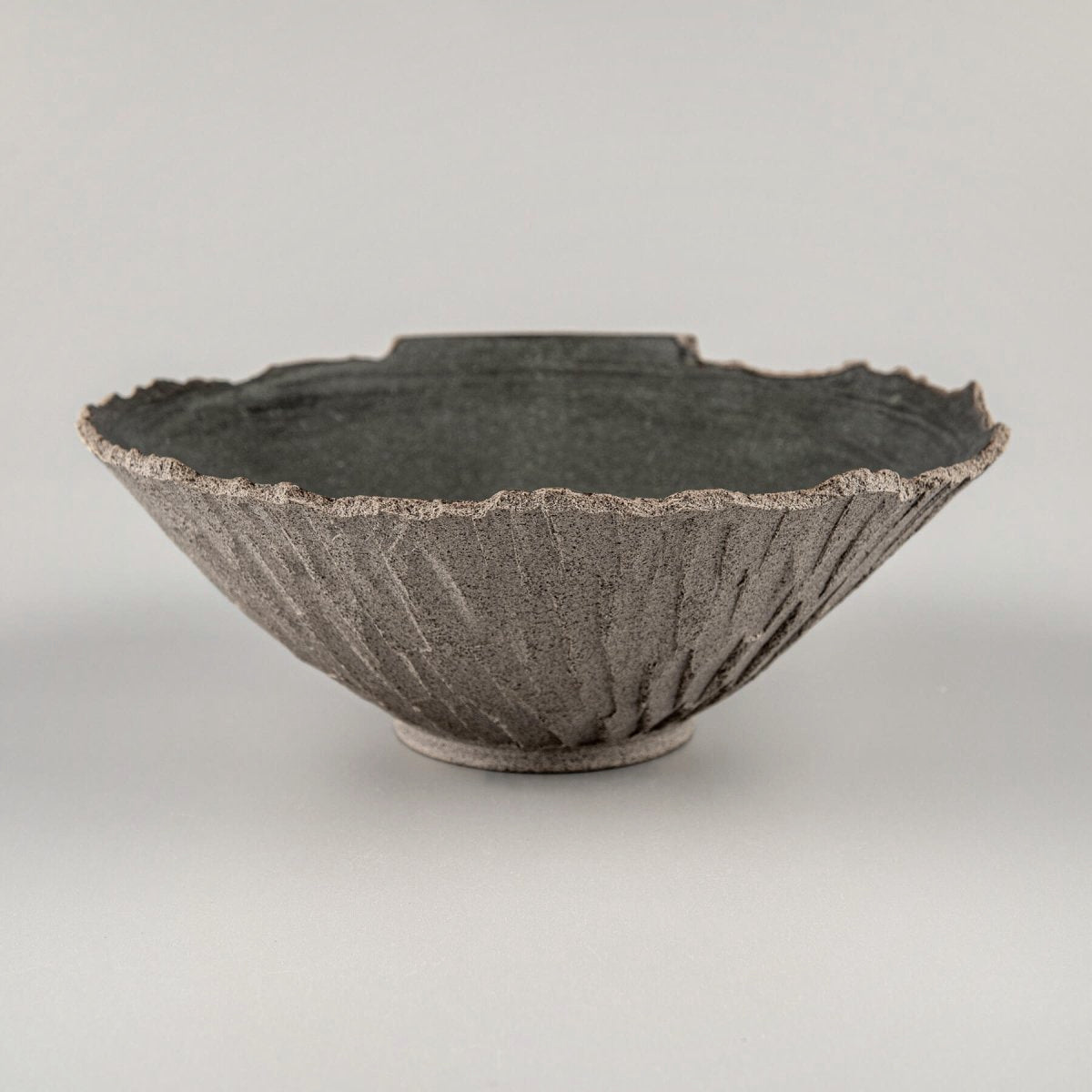 Profile of artisanal bowl with rough exterior and flared form, suited for boutique hotel interiors.