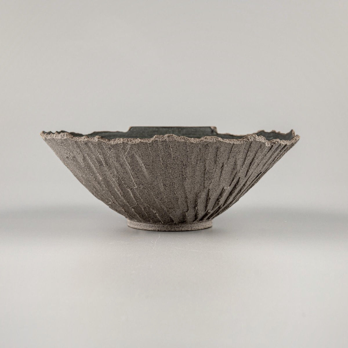 Side angle showing rustic texture of hand-carved ceramic bowl, crafted for fine dining presentation.