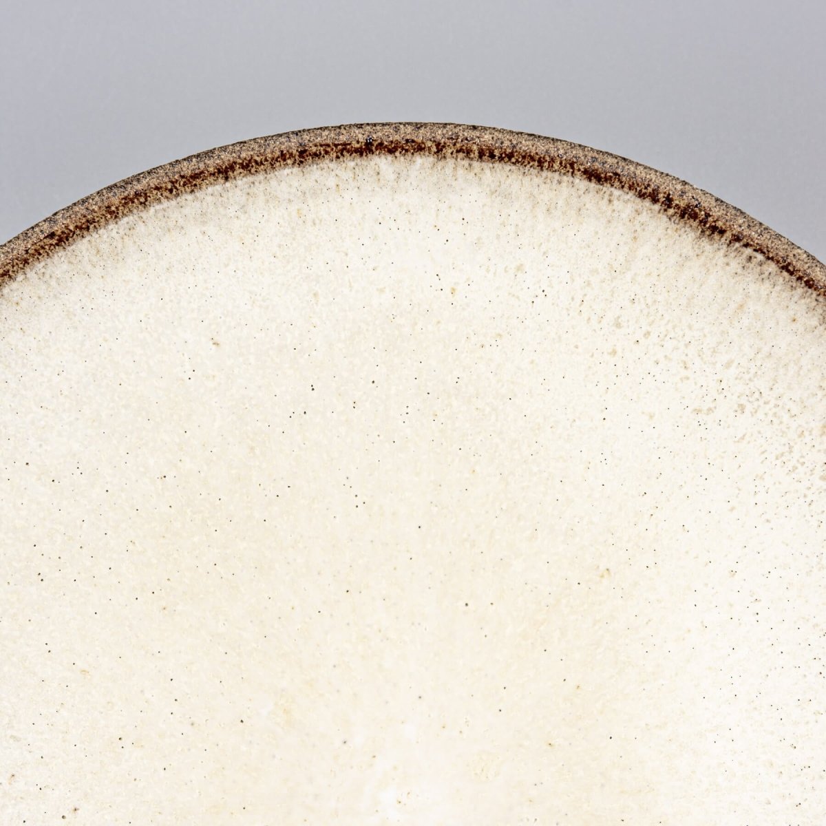 Close-up of artisanal ceramic plate showcasing textured stoneware exterior and minimalist design.