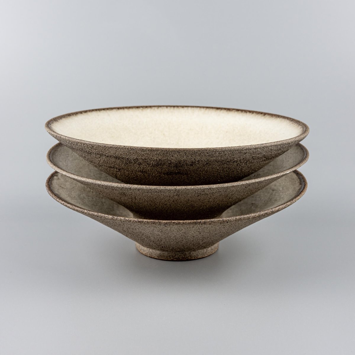 Stacked artisanal ceramic plates with white glaze interiors and stoneware exteriors.