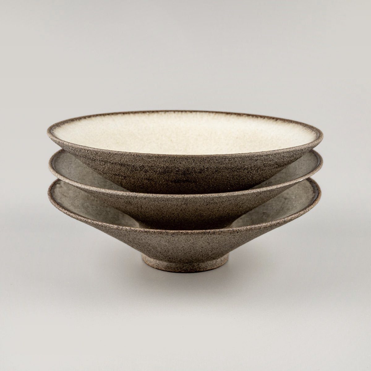 Stacked artisanal ceramic plates with white glaze interiors and stoneware exteriors.