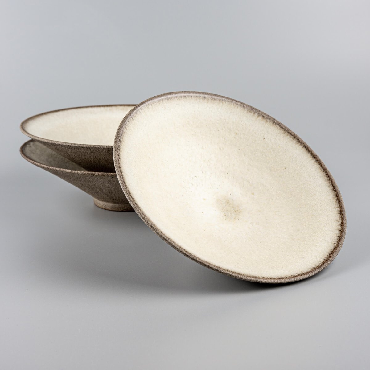 Stacked artisanal ceramic plates with white matte glaze interiors and textured stoneware exteriors for fine dining.