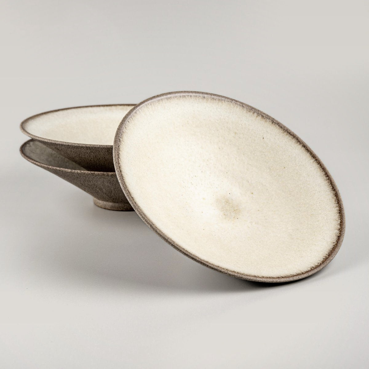 Stacked artisanal ceramic plates with white matte glaze interiors and textured stoneware exteriors for fine dining.
