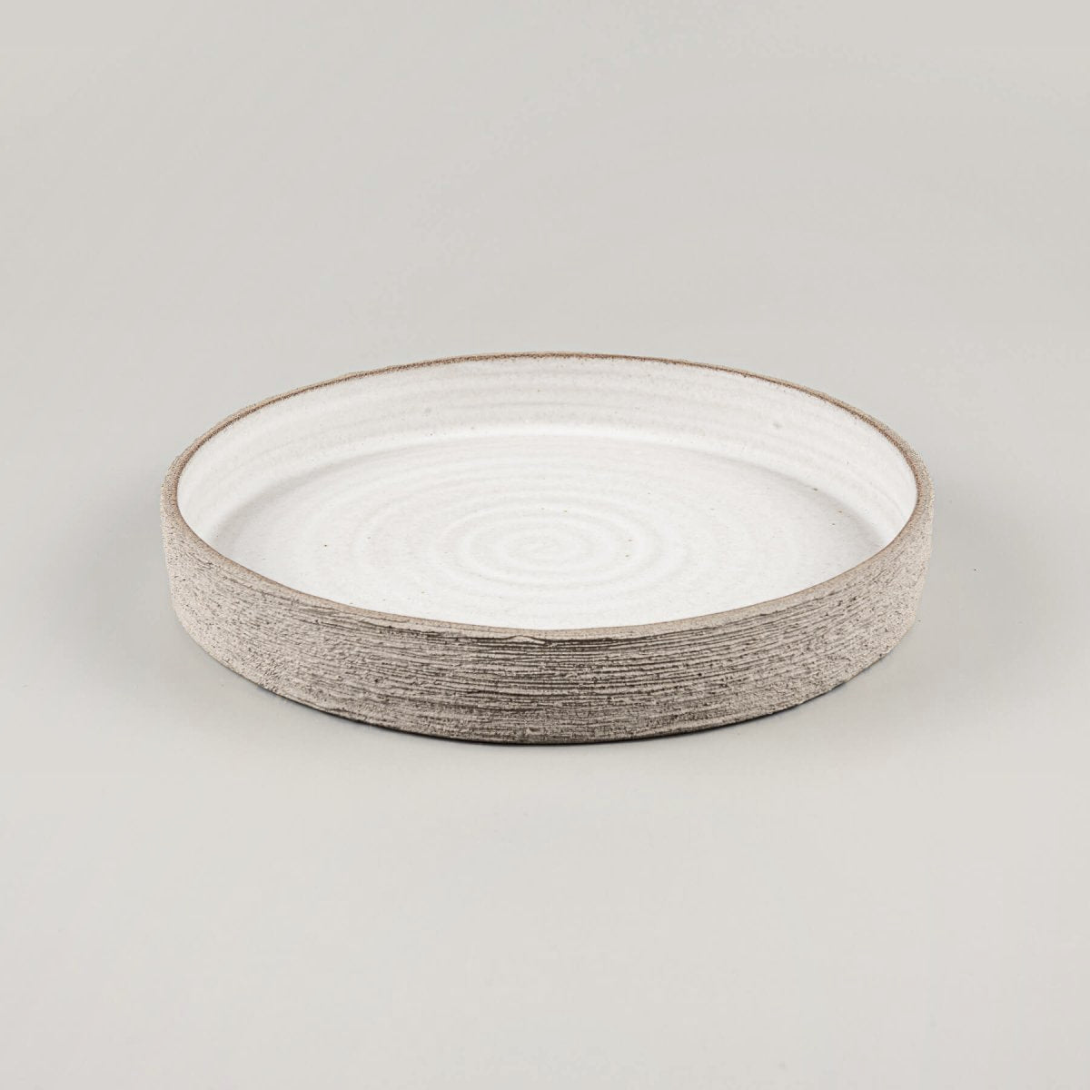 Artisan ceramic plate showcasing refined craftsmanship and an unglazed textured outer surface.