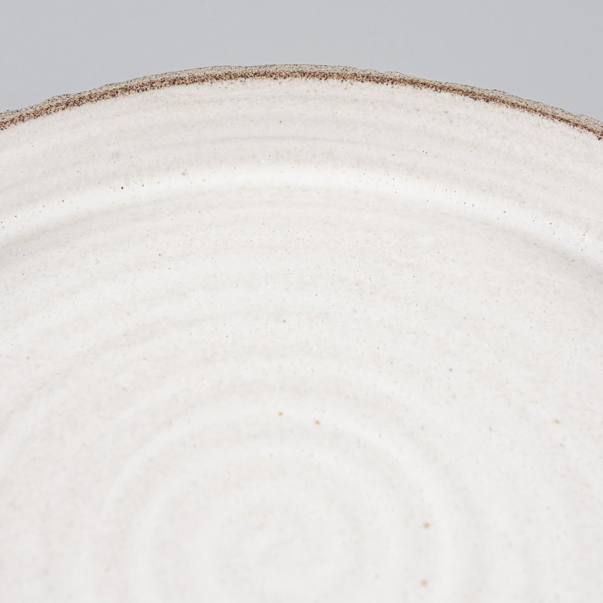 Flat handcrafted ceramic plate with minimalist spiral pattern and straight-sided profile for chefs.