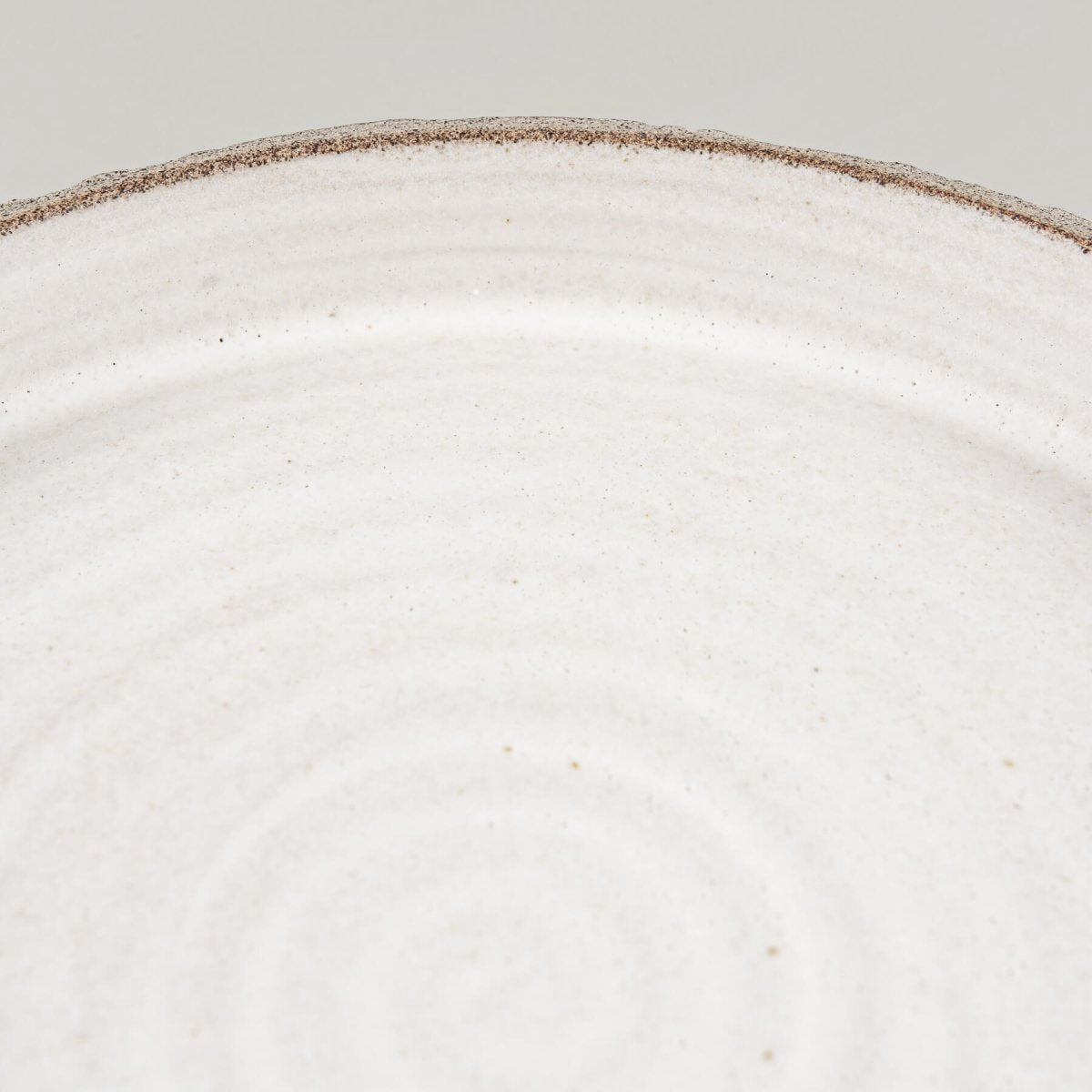 Flat handcrafted ceramic plate with minimalist spiral pattern and straight-sided profile for chefs.