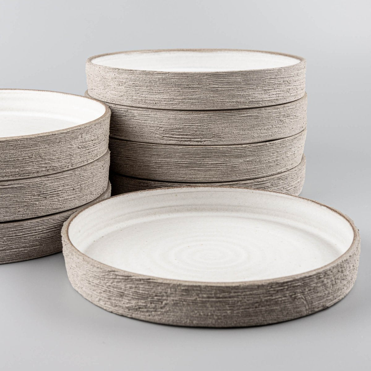 Stack of handmade ceramic plates with flat bases and spiral interior design for premium restaurant service.