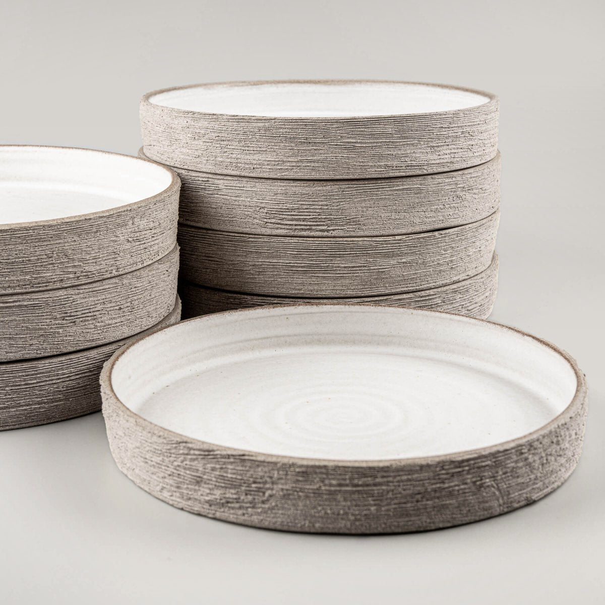 Stack of handmade ceramic plates with flat bases and spiral interior design for premium restaurant service.