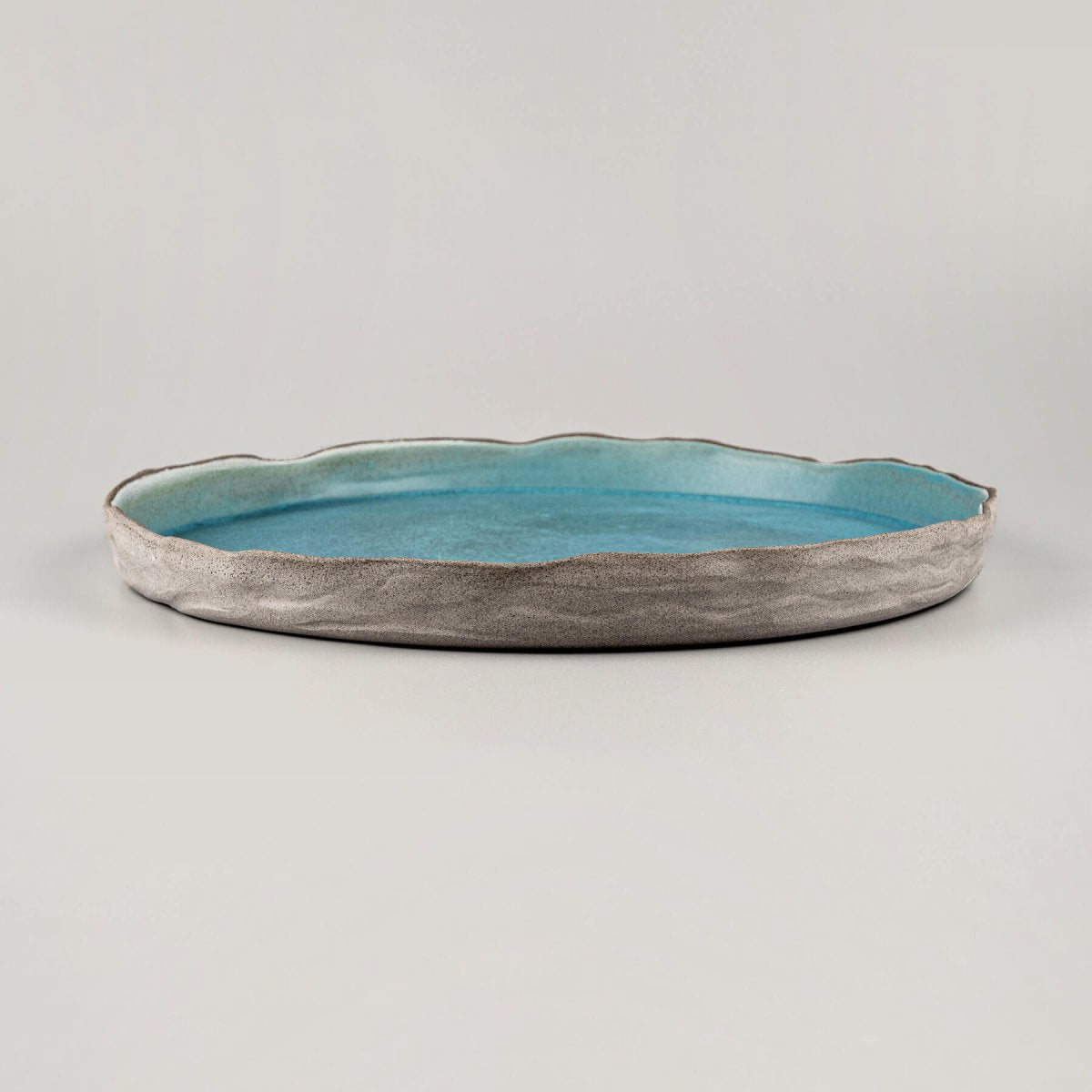 Elegant turquoise handmade dinner plate with textured unglazed exterior for premium culinary presentation.