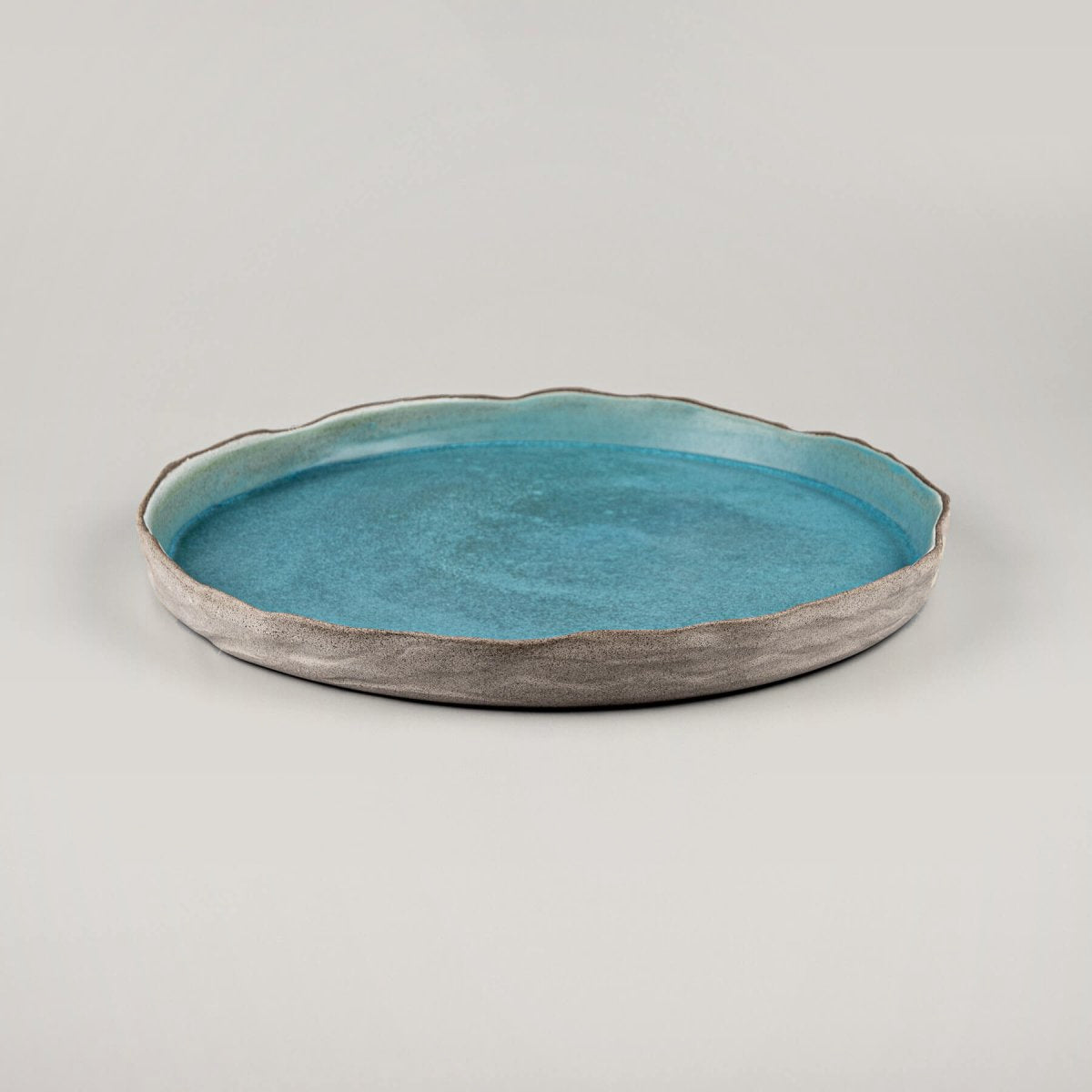 Side view of handmade dinner plate in ocean-inspired turquoise with refined beveled edges.