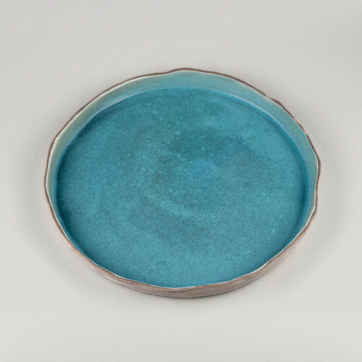 Close-up of turquoise handmade dinner plate with artistic wave-like edge detail for luxury restaurants.