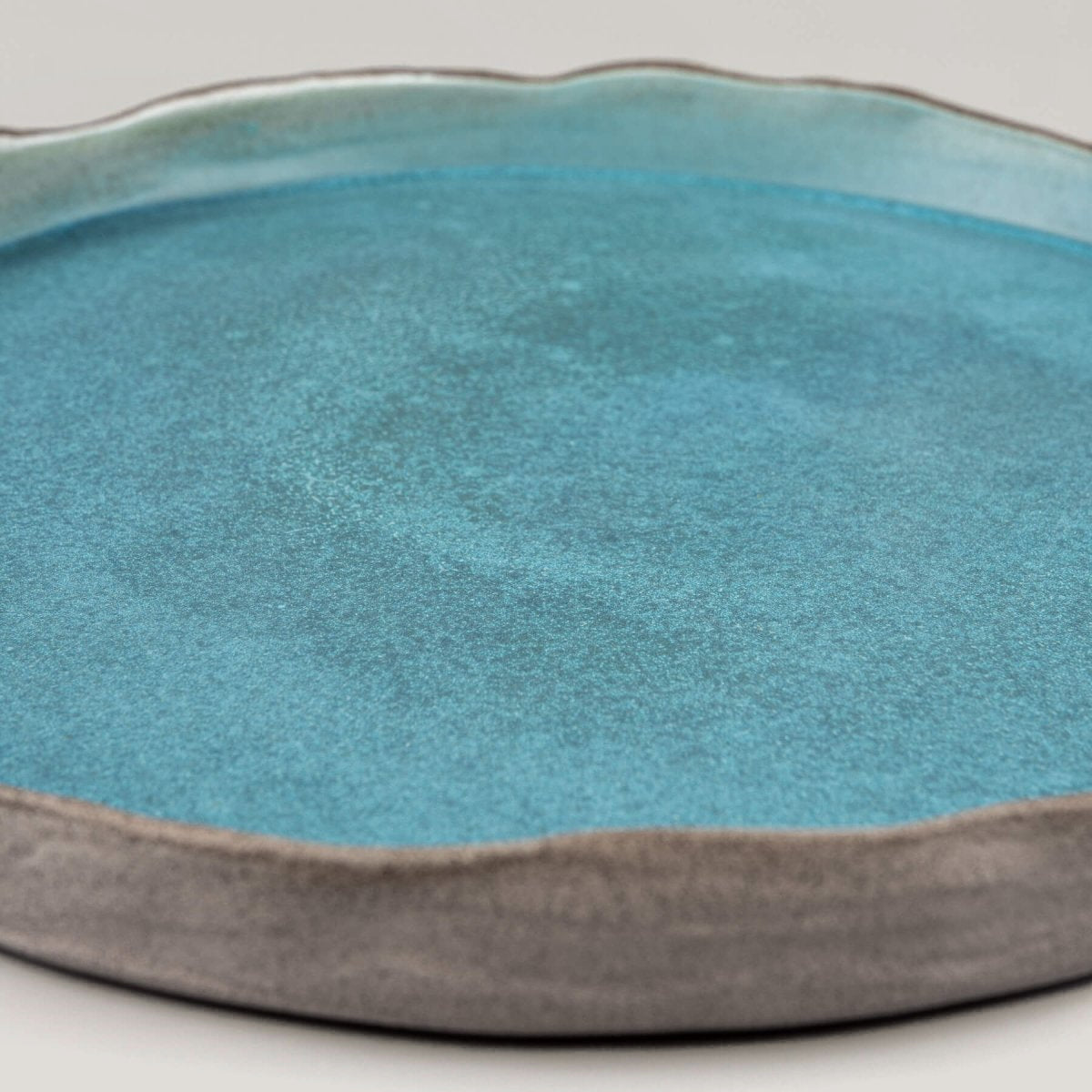 Detail of handmade dinner plate edge with organic wave form and subtle white accent for fine dining.