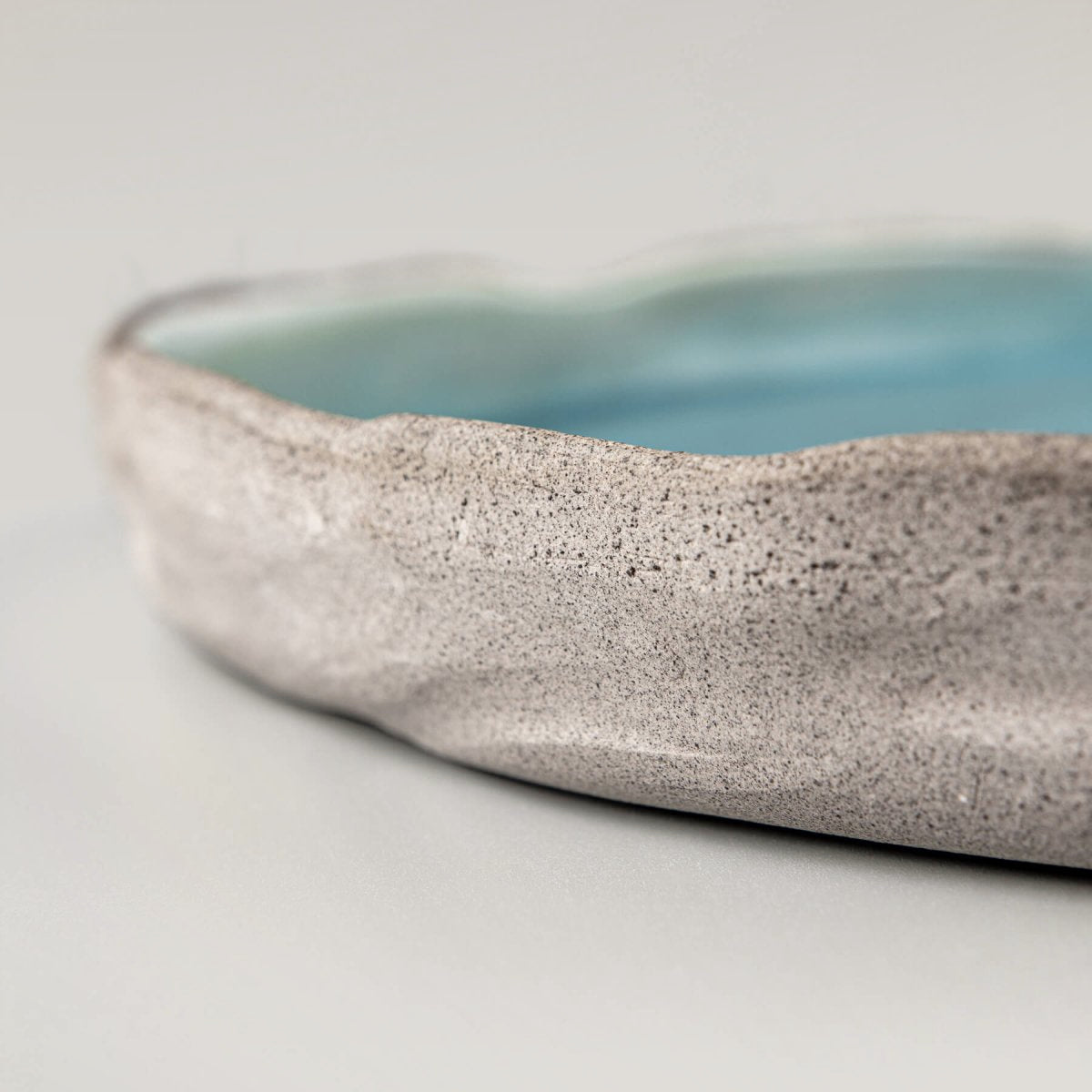 Handmade dinner plate with unglazed textured stoneware exterior and matte turquoise glazed interior for luxury fine dining.