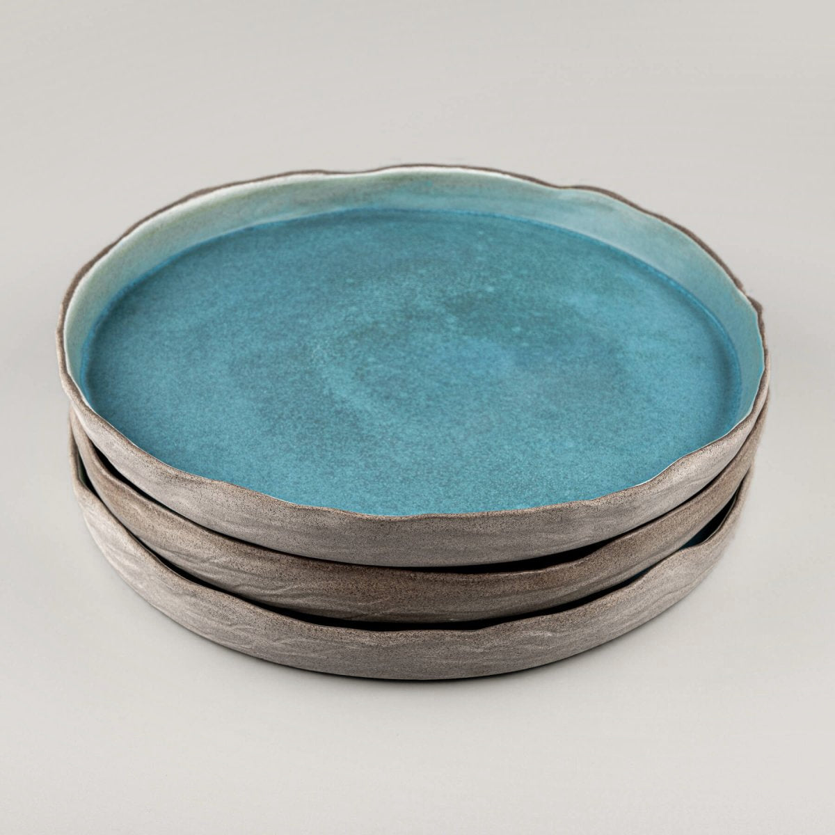Stack of turquoise handmade dinner plates with refined edges for high-end dining.