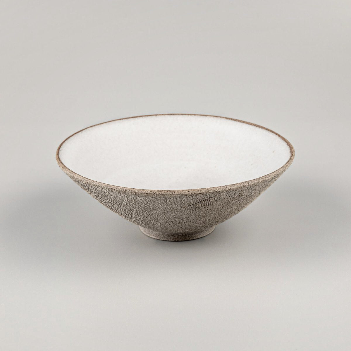 Elevated handmade ceramic bowl with carved brown exterior and glazed interior.