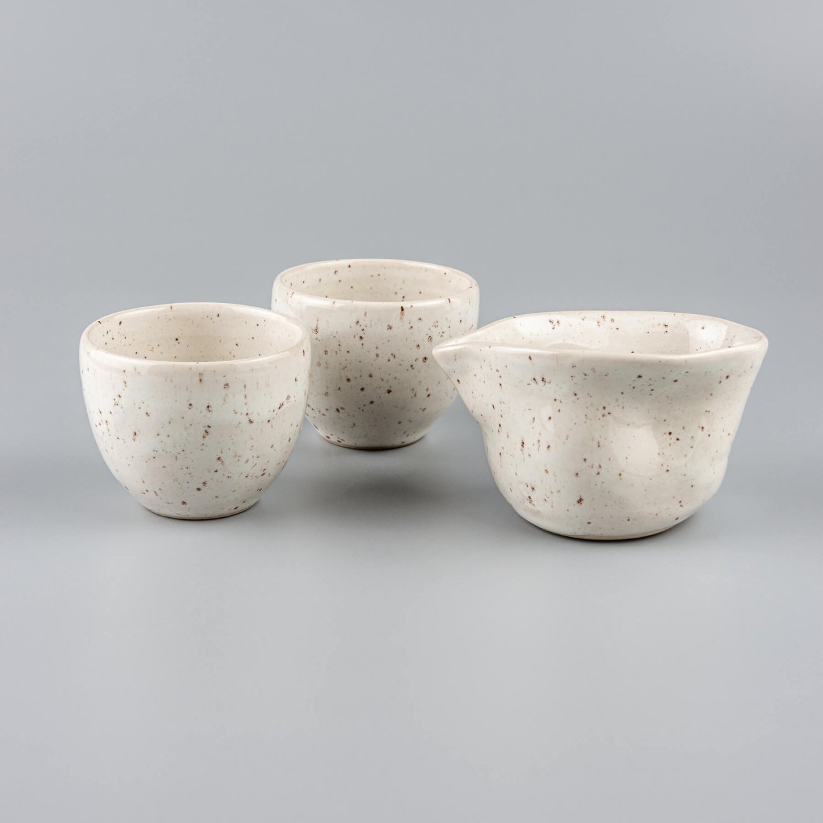 Two artisanal stoneware coffee cups stacked beside an ivory-glazed milk pitcher, perfect for restaurants and boutique hotels.