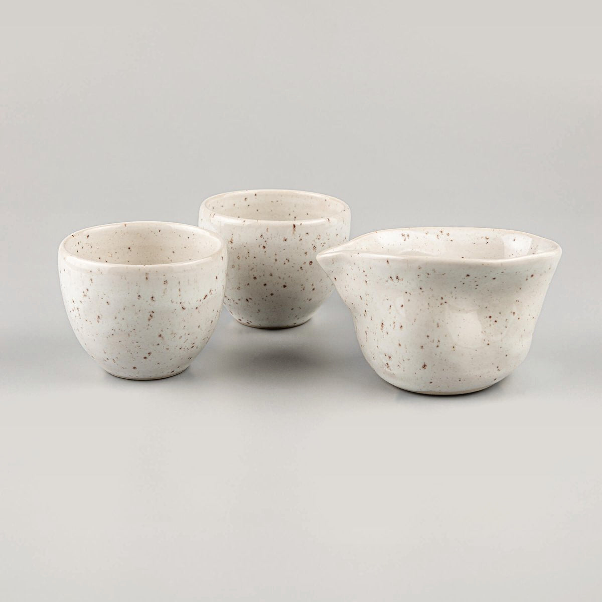Two artisanal stoneware coffee cups stacked beside an ivory-glazed milk pitcher, perfect for restaurants and boutique hotels.