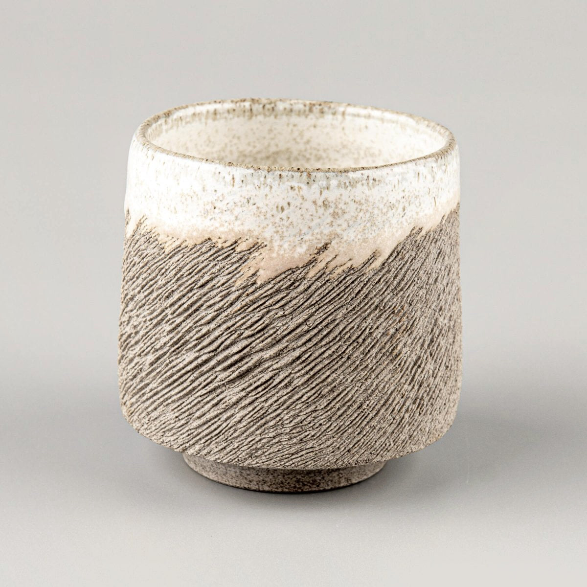 Rustic artisanal stoneware coffee cup with textured surface and white glazed rim, perfect for collectible pottery and decor.