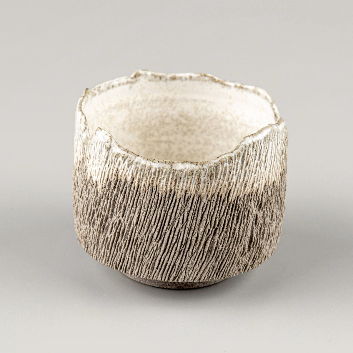 Artisan coffee cup in dark stoneware clay with irregular rim and tactile carved surface.