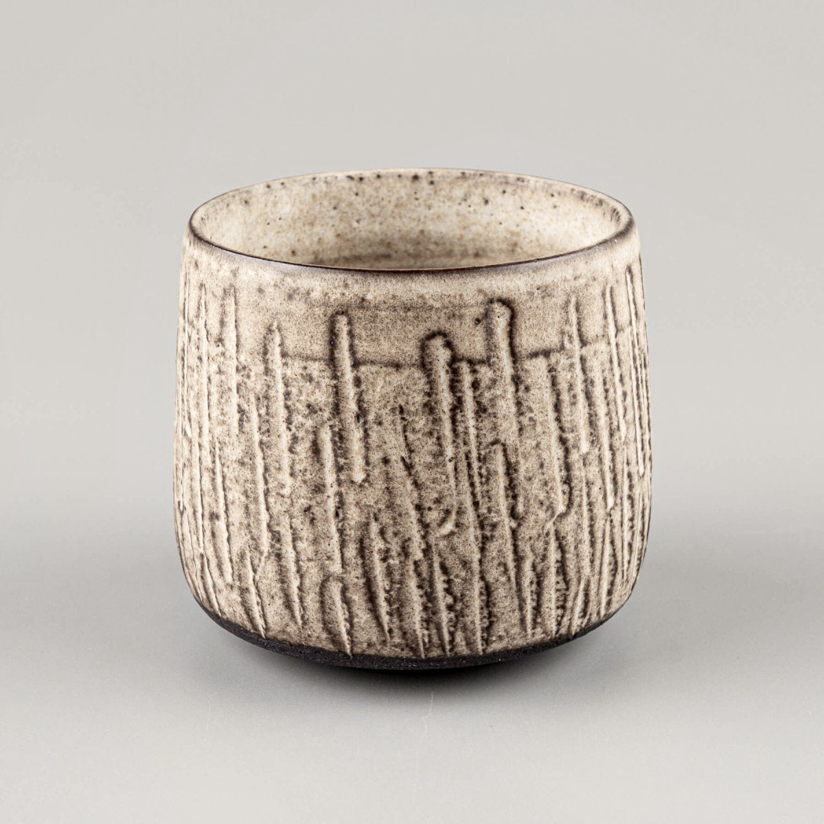 Handcrafted ceramic mugs with carved stoneware texture and matte glaze finish for modern tableware.