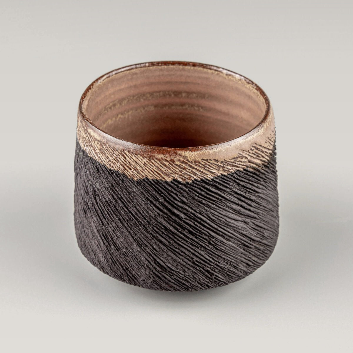 Handcrafted pottery mug in black stoneware with carved exterior and semi-gloss glazed rim, perfect for fine dining use.