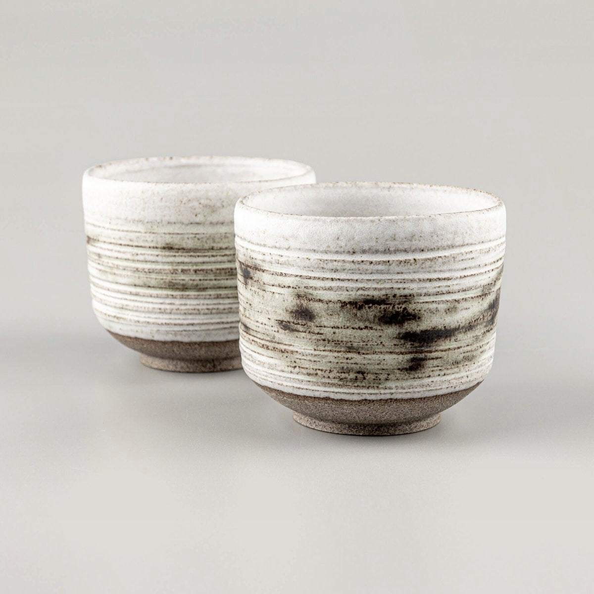 Handcrafted pottery mugs with white matte glaze and carved texture for modern tableware.