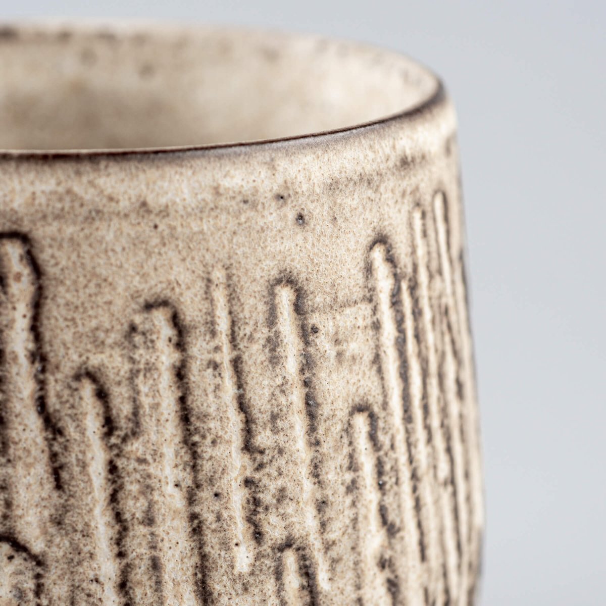 Profile view of artisan ceramic mug with carved exterior design and contemporary matte glaze.