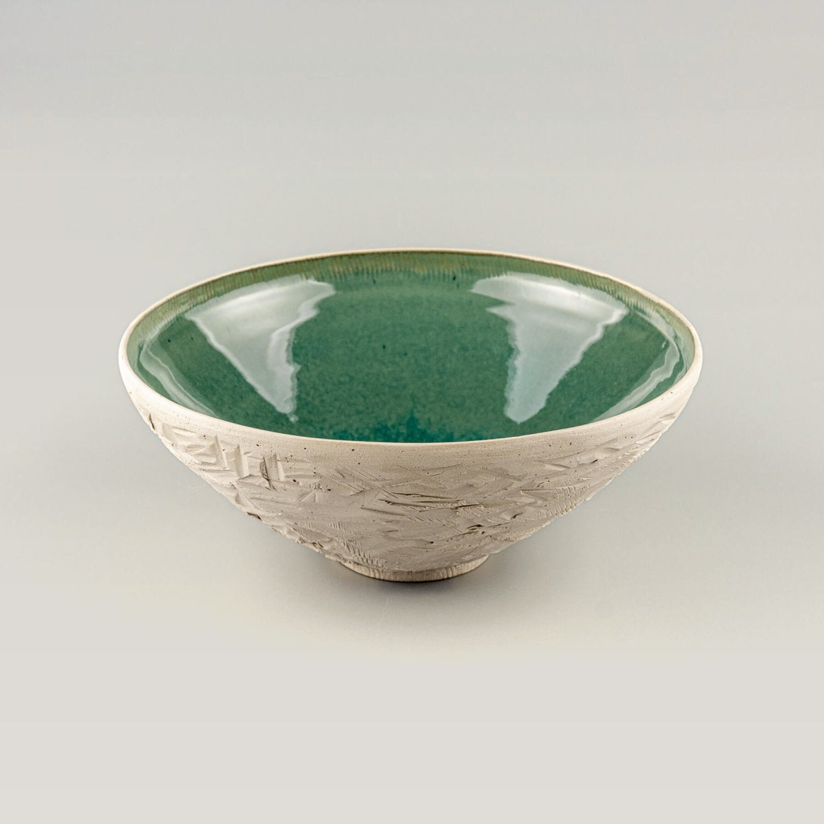 Angled side view of handmade ceramic serving bowl with textured unglazed exterior and rounded rim.