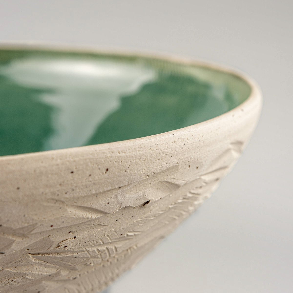 Zoomed-in corner of ceramic bowl showing glaze edge and carved outer wall.