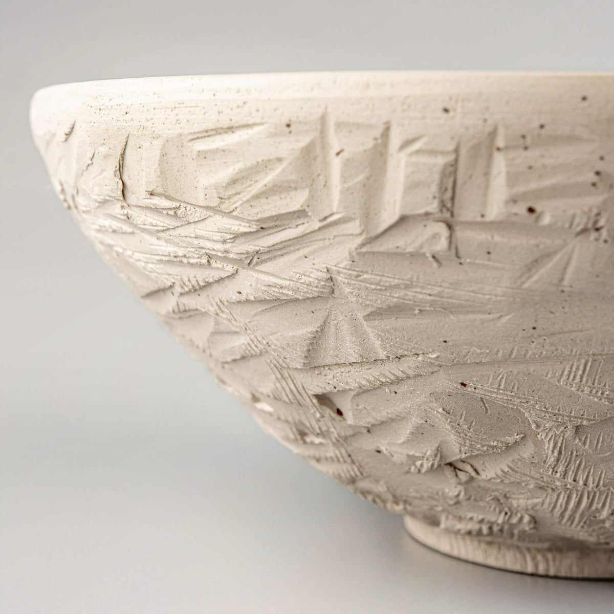 Side view of carved ceramic serving bowl with textured unglazed white stoneware exterior.